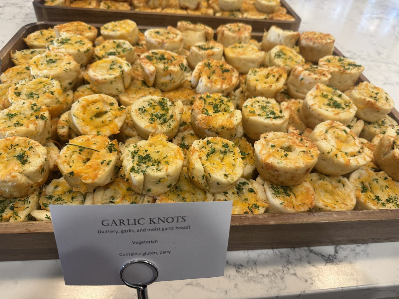 Printed dish card naming garlic knots with vegetarian and allergen information beside the tray